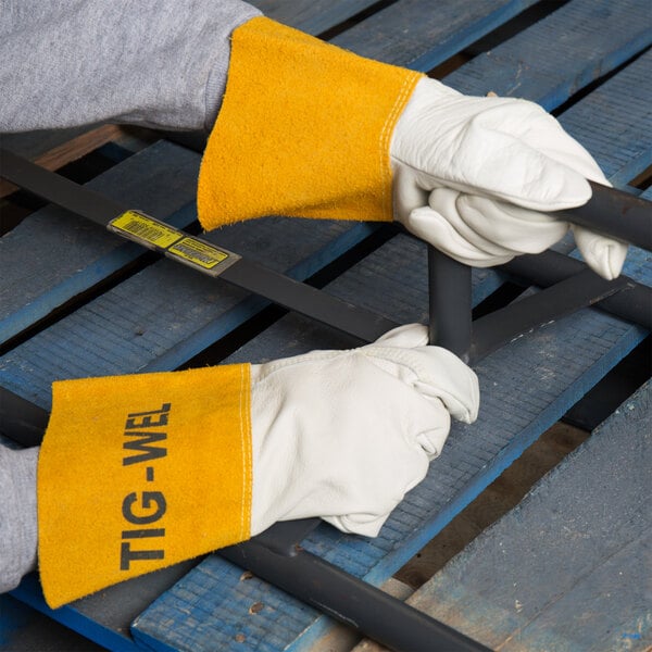 A person wearing Cordova leather welding gloves holding a metal bar.