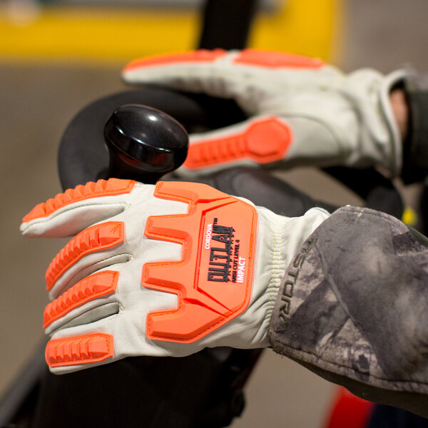 A person wearing Cordova Outlaw Impact leather gloves with orange and black TPR protectors.