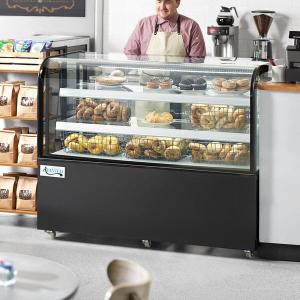 A man wearing an apron standing behind an Avantco black dry bakery display case filled with pastries.