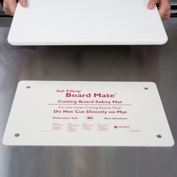 A person holding a white cutting board with a San Jamar white cutting board mat.