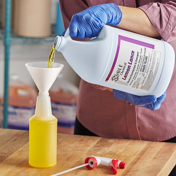 A person in blue gloves pouring yellow Noble Chemical Lemon Lance liquid into a bottle.