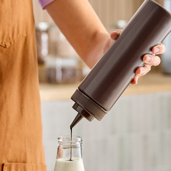 A brown 24 oz. wide mouth squeeze bottle being used to dispense liquid into a glass bottle.