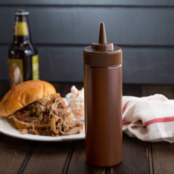 A brown Choice wide mouth squeeze bottle of sauce next to a plate of food.