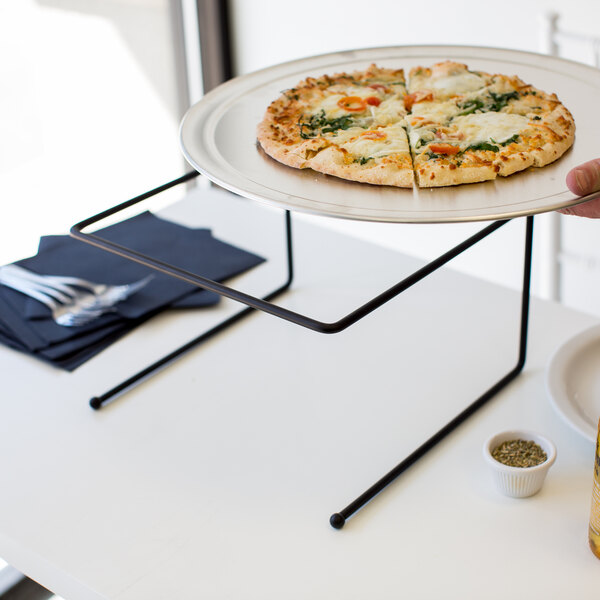 A hand holding a pizza on a black metal pizza stand.