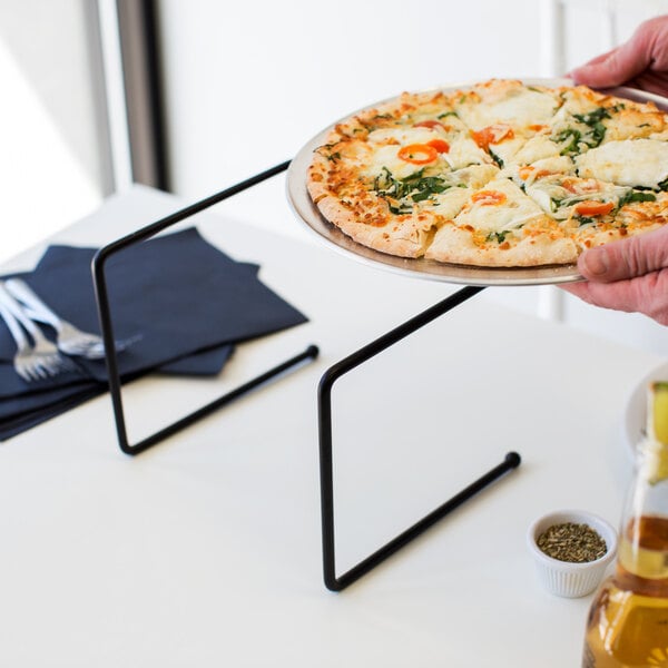 A person holding a pizza on a black metal pizza stand.