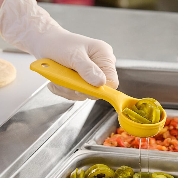 A person in gloves holding a Carlisle yellow perforated portion spoon with food in it.