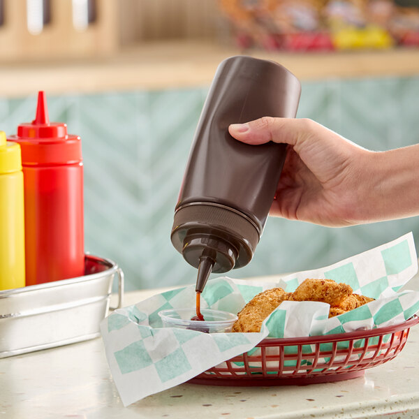 A brown 16 oz. wide mouth squeeze bottle being used to dispense sauce into a small container next to fried food.