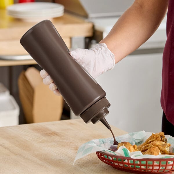 A 32 oz. brown wide mouth squeeze bottle being used to dispense sauce onto food.