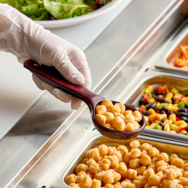 A person in gloves holding a Carlisle reddish brown portion spoon full of food over a salad bar.