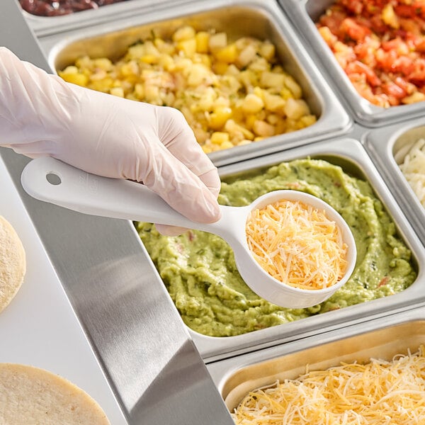 A gloved hand using a Carlisle white plastic portion spoon to serve cheese over food.