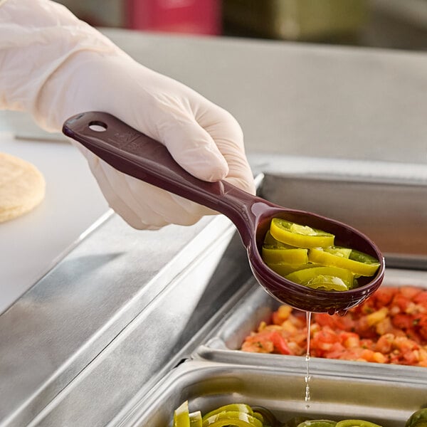 A person using a Carlisle reddish brown short handle perforated portion spoon to serve food.