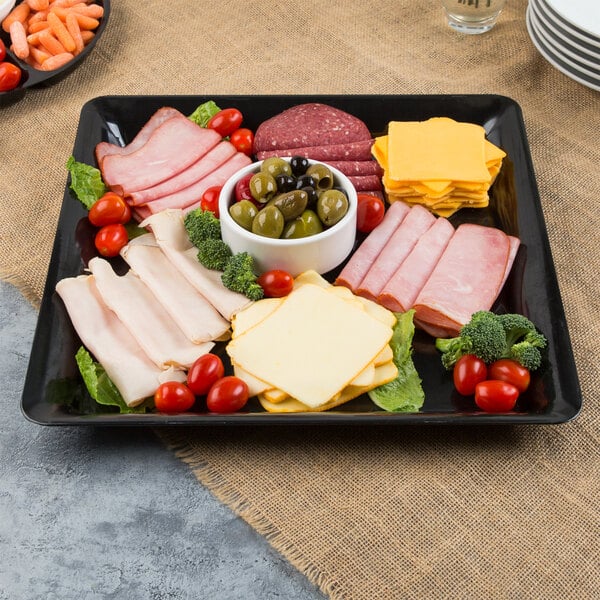 A Fineline black plastic square cater tray with meat, cheese, olives and vegetables.