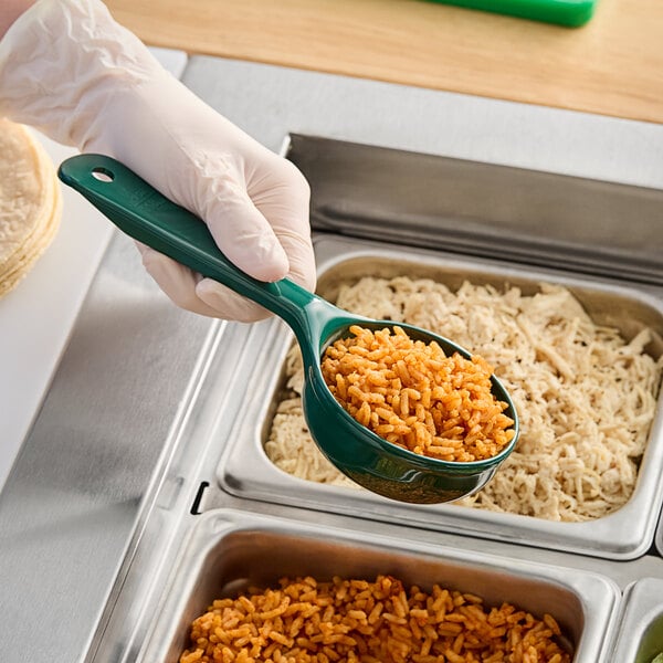 A person in gloves holding a Carlisle forest green short handle portion spoon with food in it.