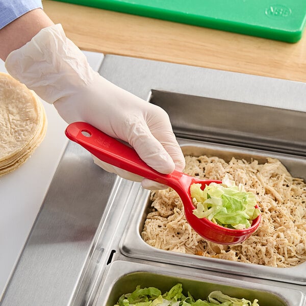 A person in gloves holding a Carlisle red short handle portion spoon of food.