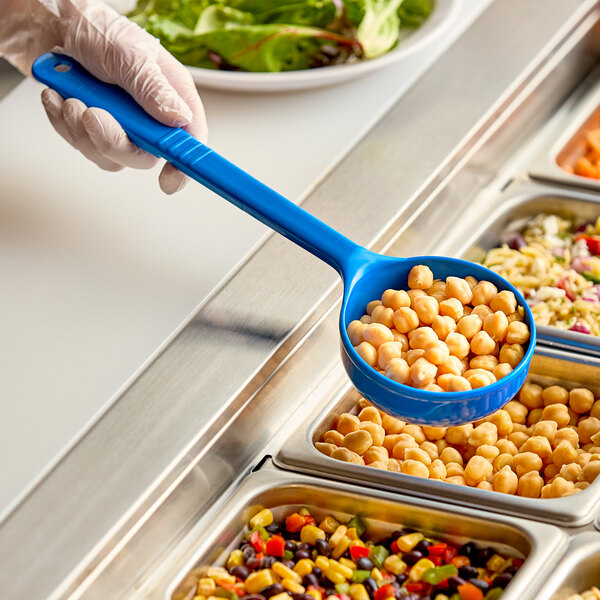 A person holding a Carlisle blue acetal long handle portion spoon over a bowl of food on a counter.