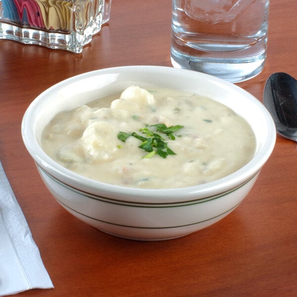 A Tuxton Green Bay china bowl filled with soup with a spoon.