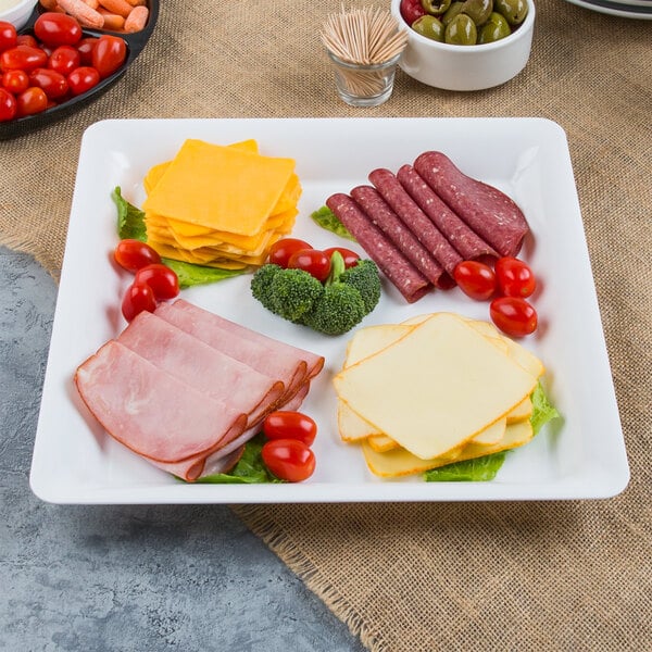 A Fineline white plastic square cater tray with cheese, meat, and vegetables.