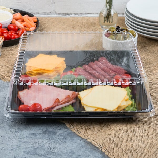 A Fineline black plastic square catering tray with meat, cheese, and vegetables on a table.