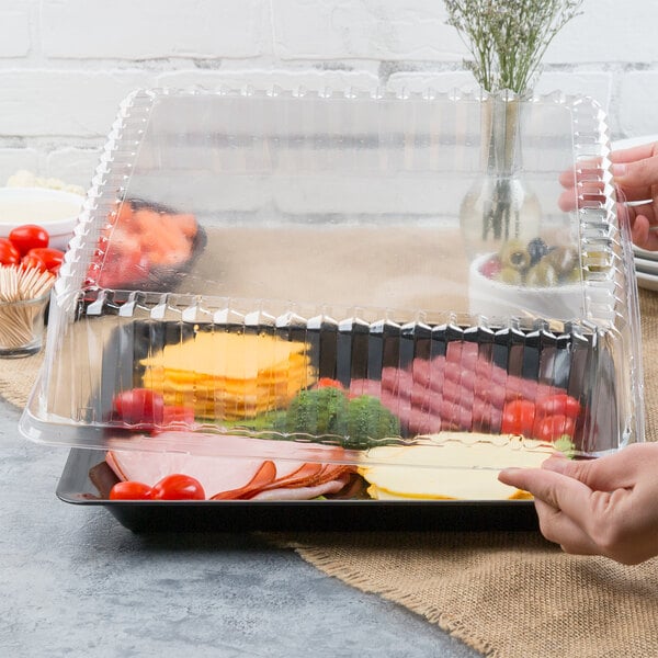 A hand holding a Fineline clear plastic container with a tray of food and a clear plastic lid.