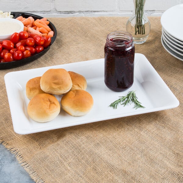 A Fineline white rectangular plastic catering tray with rolls and a jar of jam on it.