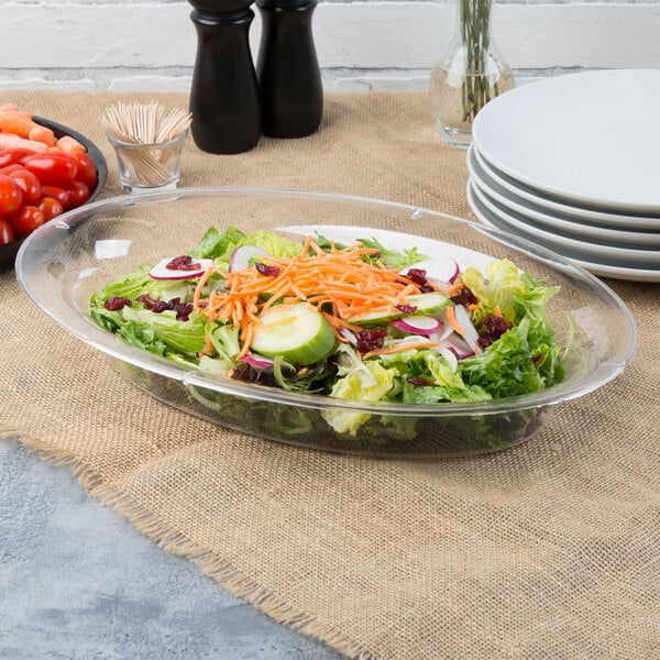 A salad in a clear Fineline oval catering bowl with cucumbers and carrots.