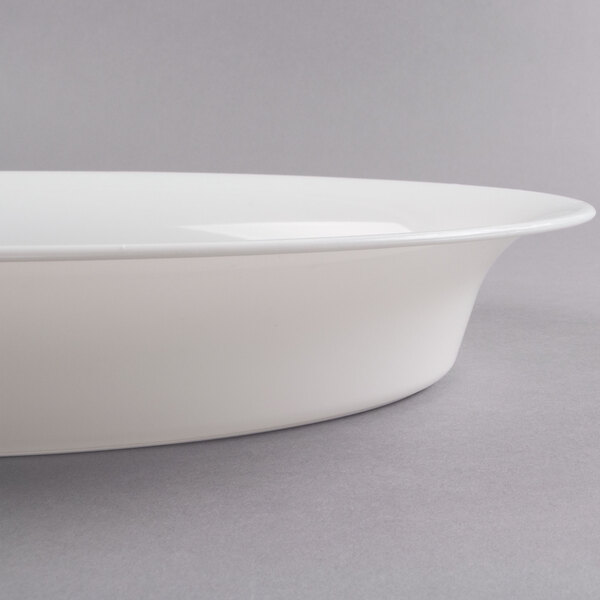 A close-up of a white Fineline oval catering bowl with a rim on a gray surface.