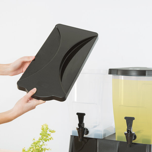 A person holding a black rectangular lid over a yellow liquid in a clear container.