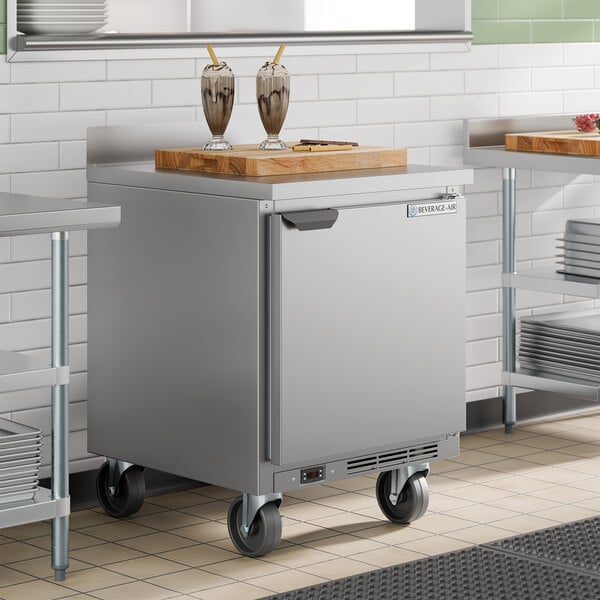 A stainless steel single door worktop freezer on casters with a cutting board and two milkshakes on top.