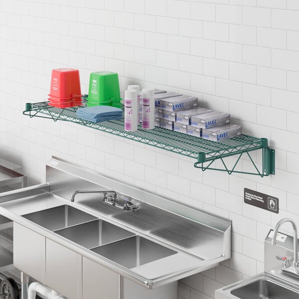 A Regency green epoxy wire wall mount shelf above a stainless steel sink with a faucet.