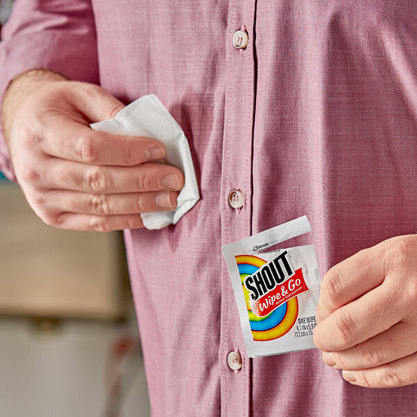 A man holding a small packet of SC Johnson Shout Instant Stain Remover Wipes.