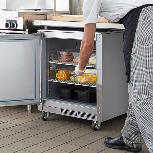 A man putting food into a Beverage-Air undercounter refrigerator in a kitchen.