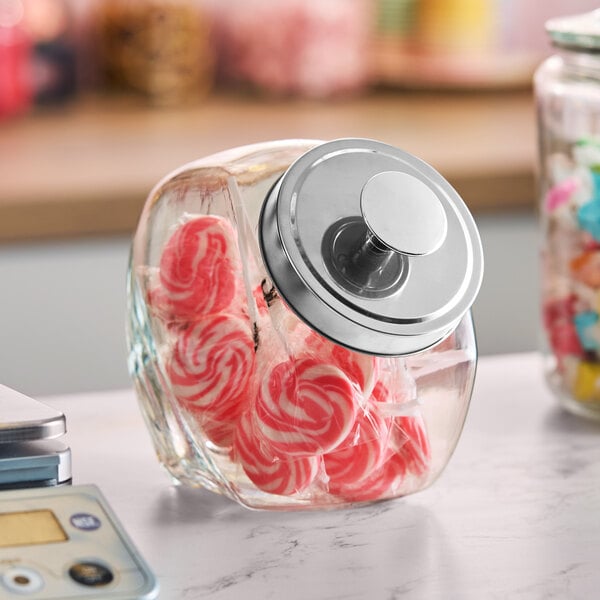 A glass penny candy jar with a chrome lid, partially filled with red and white candies.