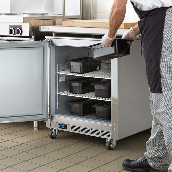 A man in a black apron putting a black rectangular plastic container in a white Beverage-Air undercounter freezer.