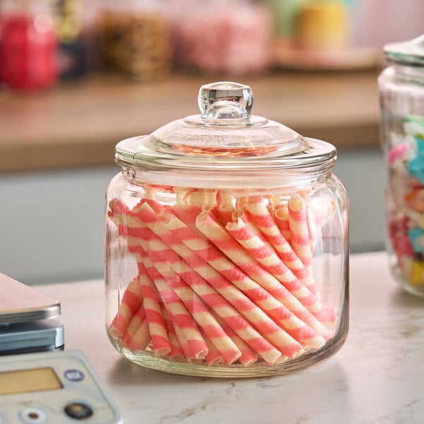 A clear glass jar with a lid, filled with pink and white striped wafer rolls.