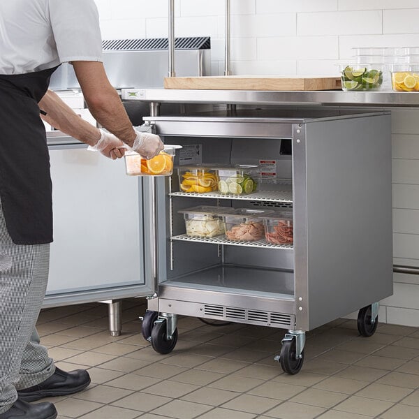 A man in a school kitchen putting food into a Beverage-Air undercounter refrigerator.