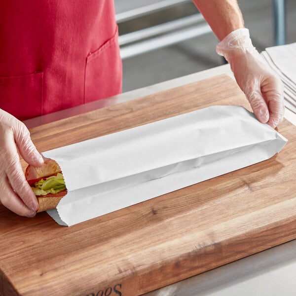 A person in a red shirt and white gloves holding a sandwich in a white Bagcraft Packaging bread bag.