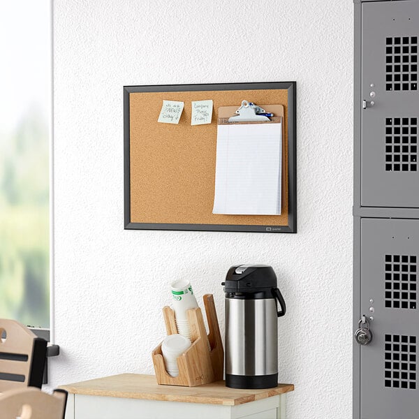 A Quartet cork board with a note on it and a black aluminum frame.