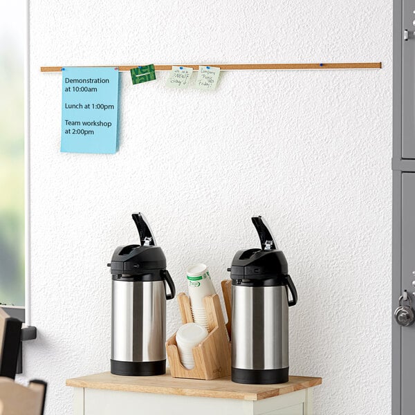 A Quartet cork bulletin bar with two coffee cups and a water bottle on a shelf.