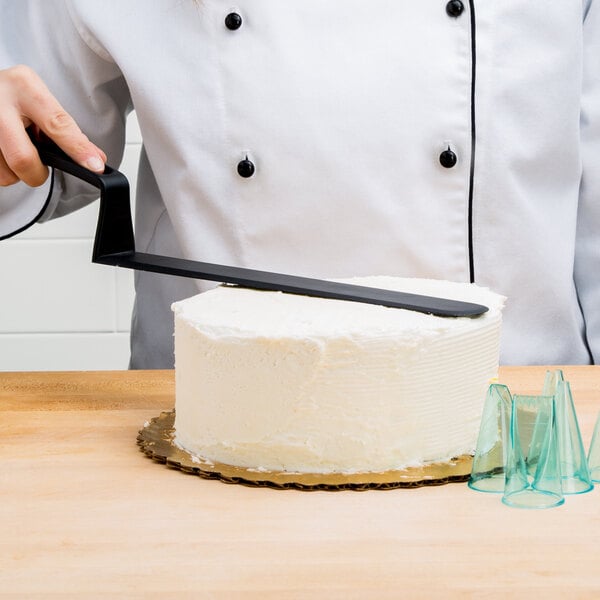 A person using a Matfer Bourgeat offset spatula with a white handle to cut a white cake.