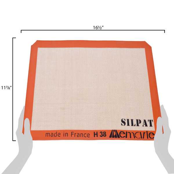 A hand holding a measuring tape with the word "SILPAT" on it, measuring 11 5/8" x 16 1/2"