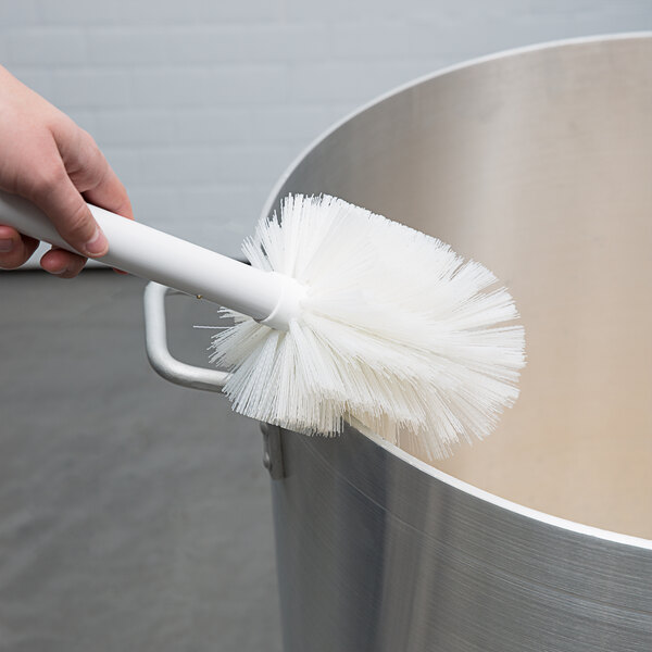 A hand holding a Carlisle white multi-purpose cleaning brush over a silver container.