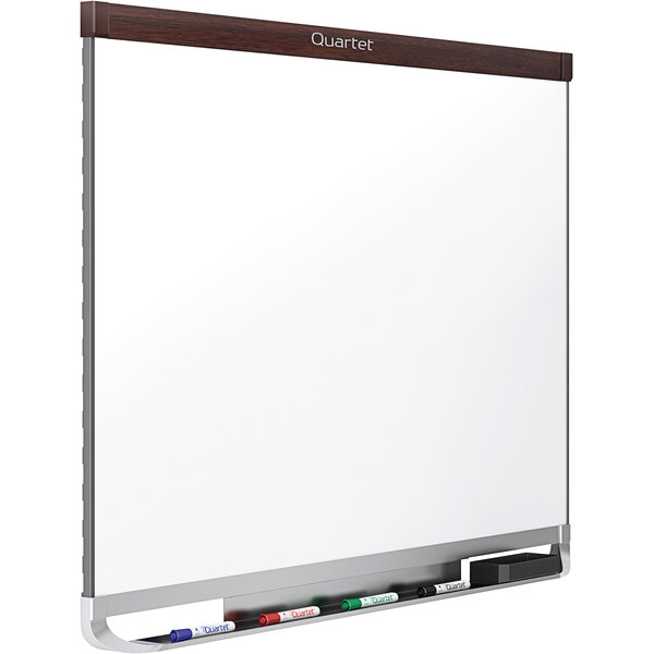 A Quartet magnetic porcelain whiteboard with a mahogany plastic frame and black marker holder.