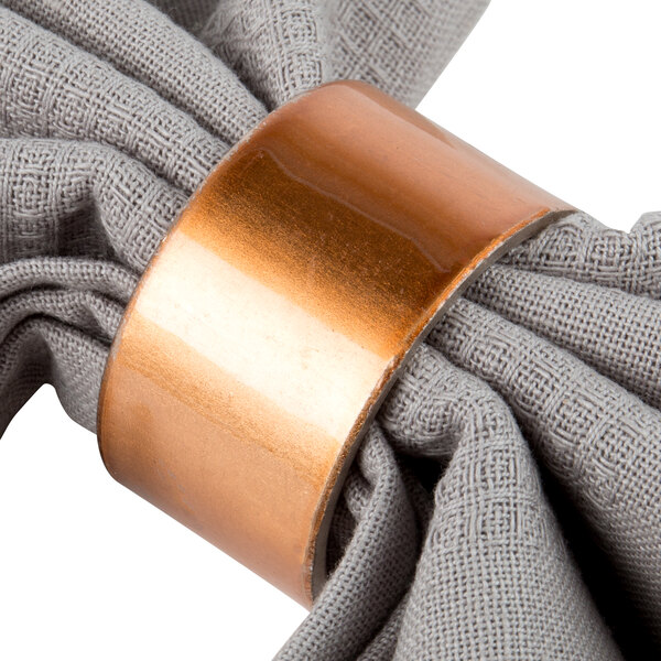 A table set with a white napkin in a copper napkin ring.