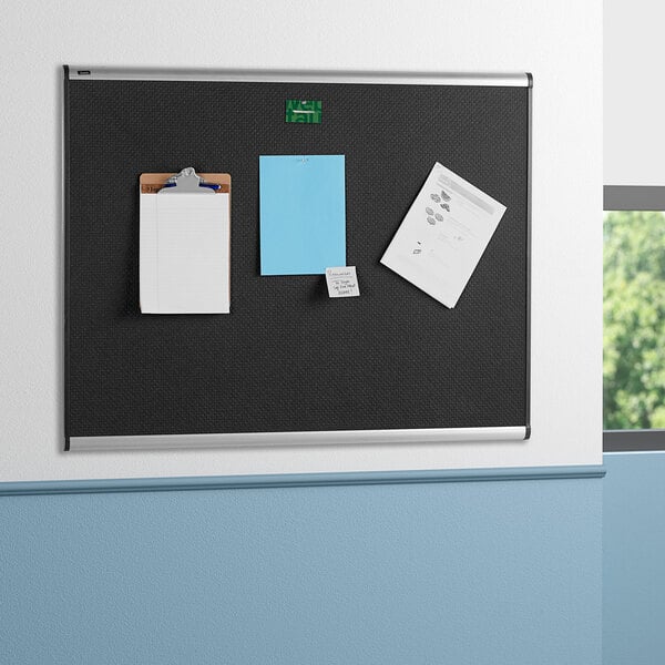 A black Quartet embossed foam bulletin board with papers and notepads on it.
