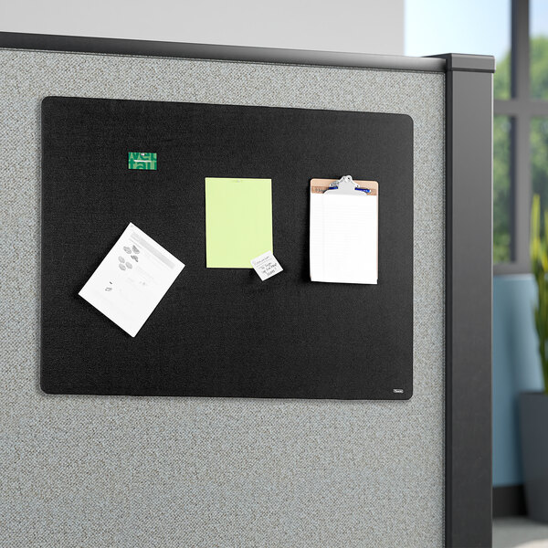 A black Quartet fabric bulletin board with papers and notes on it.