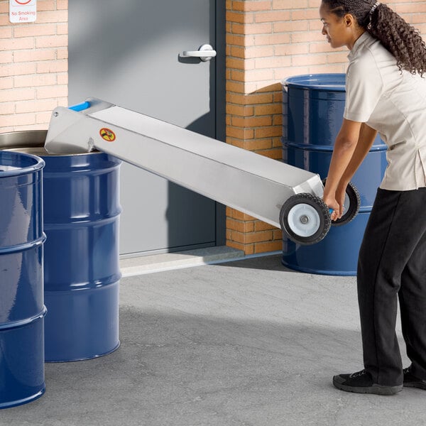 A stainless steel Shortening Shuttle SS-709 70 lb. waste oil transport container being used to transfer oil into a blue drum.
