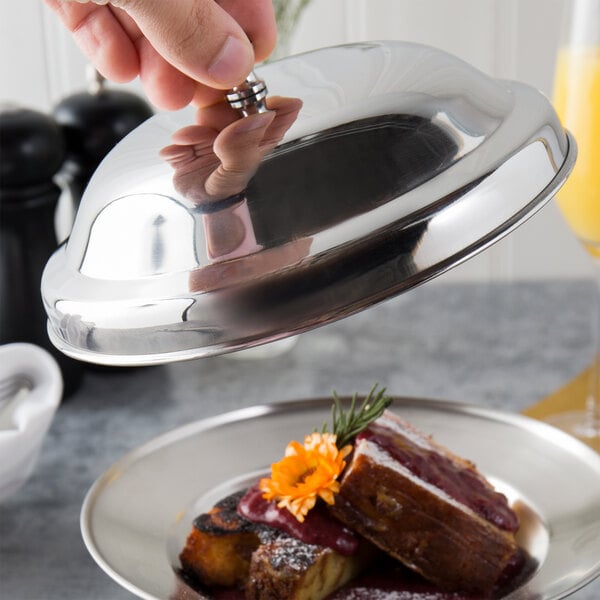 A hand holding a Town stainless steel cloche over a plate of food.