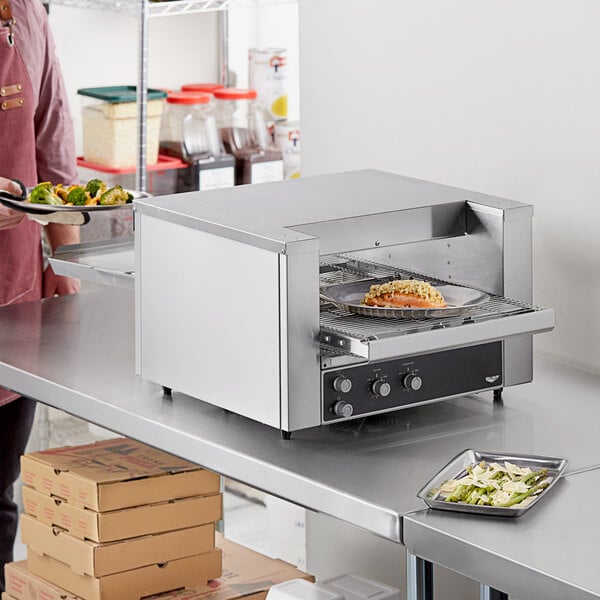 A man using a Vollrath ventless countertop conveyor oven to cook food on a table.