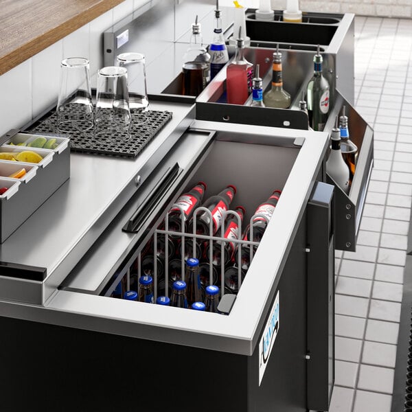 An Avantco black horizontal bottle cooler on a counter filled with bottles.