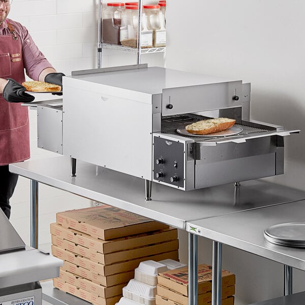 A man using a Vollrath countertop conveyor oven to cook bread in a commercial kitchen.